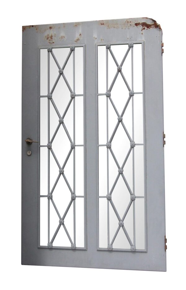 Gray steel entry door with two tall glass panels, diamond lattice design, and floral rosettes, shown with visible rust along the top edge and hardware on the left side.