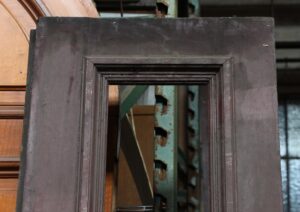 Close-up of an antique narrow door with a long vertical opening and layered molding around the glassless panel.