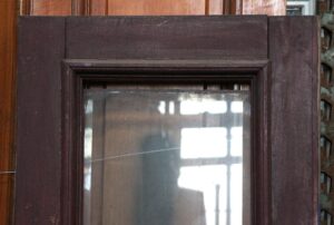Close-up of a wooden door with a narrow beveled glass panel and two wood panels, shown in a dark wood tone.