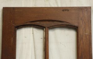 Close-up of a dark wood tone door frame with arched glass cutouts, showing the upper section and four-panel design without installed glass.