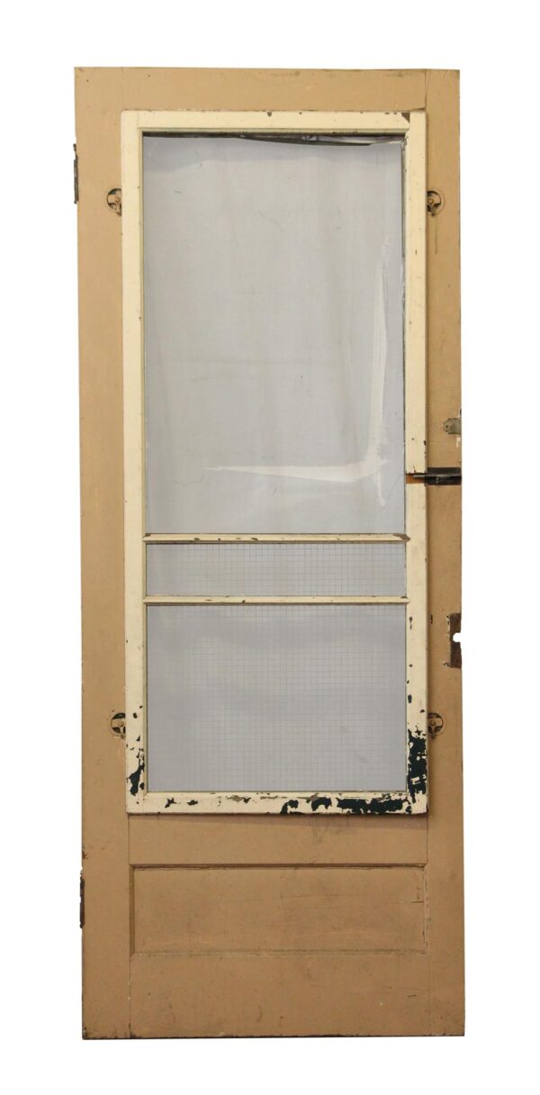 Old two-panel screen door with a tan painted frame, glass or screen inserts, and some intact hardware visible.