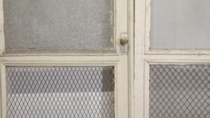 1940s white wood screen double doors with two glassless upper panels and wire-mesh lower panels, shown in a close-up of the center seam and latch.