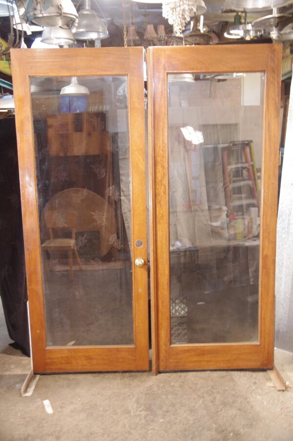 Double oak patio doors with a medium wood tone finish and one large vertical glass pane in each door, shown closed with the hardware visible at center.