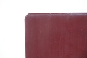 Close-up of a red glass sheet with a chipped top corner and worn edges.