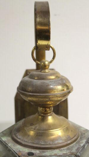 Close-up of the brass lantern sconce finial and top section with aged antique brass finish.