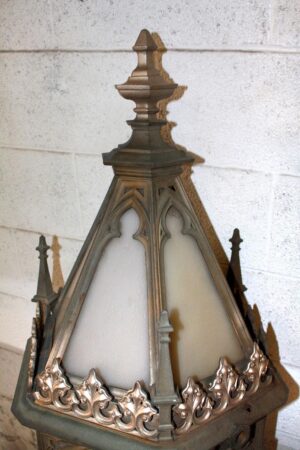 Gothic exterior sconce with a pointed finial and arched glass panels in a close-up view of the upper section.