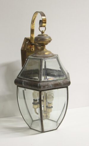 Traditional exterior lantern wall sconce with antique brass finish and beveled glass, shown front view with three visible bulb sockets.