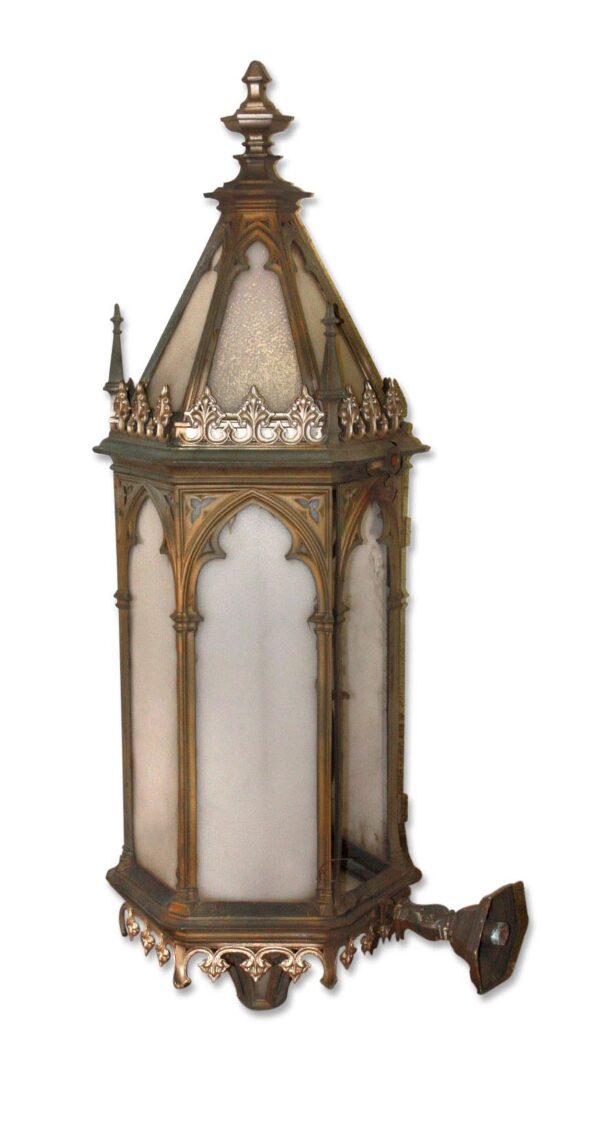 Gothic exterior sconce with a pointed top, arched panels, and an attached light fixture arm.