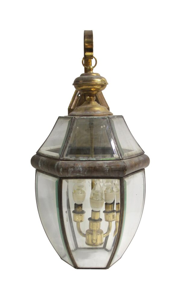 Traditional exterior lantern wall sconce with antique brass finish and clear beveled glass, shown with three candle-style lights and a hanging loop at the top.