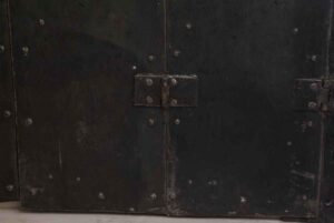 Close-up of a steel bi-fold shutter pair showing the hinged center seam and cast iron hardware with rows of rivets.