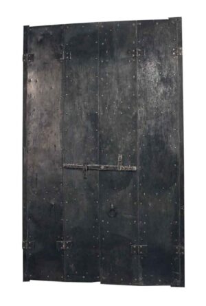 Pair of steel bi-fold shutters shown closed, with riveted panels and a cast iron drop bar latch bolt lock on one side.