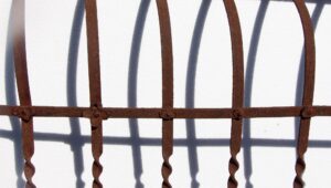 Close-up of a reclaimed wrought iron railing section with vertical bars, a horizontal brace, and small floral details between the joints.