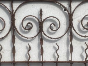 Close-up of a wrought iron fence section with circular scrollwork and vertical finials, shown as a decorative panel.