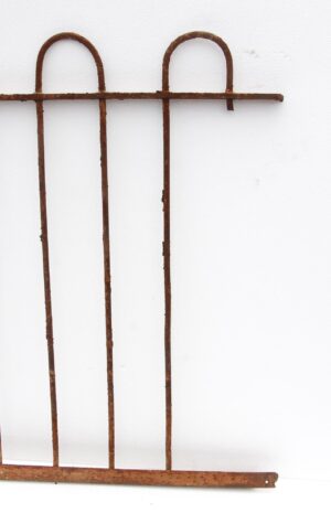 Heavily rusted wrought iron fence section with looped bars and a missing section on the right side.