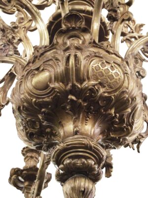 Close-up of an ornate French bronze chandelier with scrolling Rococo details, showing the central column, several curving arms, and a decorative bottom finial.