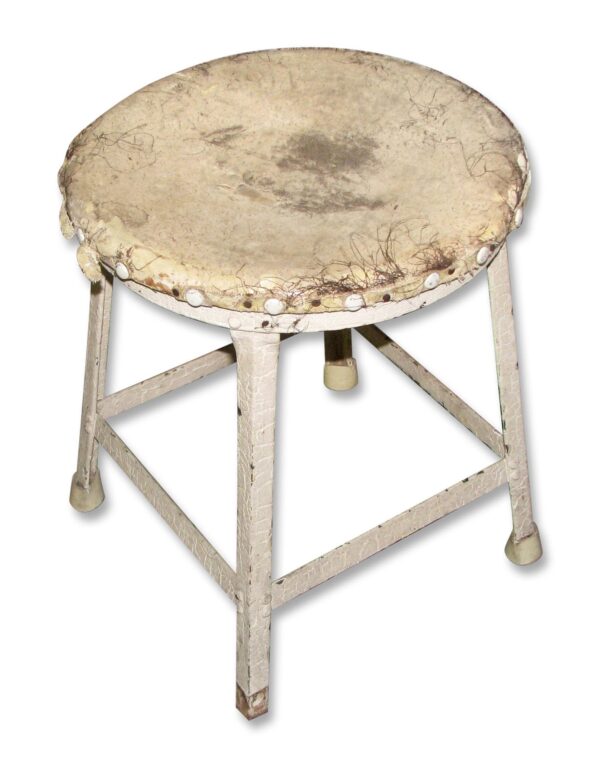 Vintage white metal step stool with a worn, torn seat and three legs visible from a slight angle.