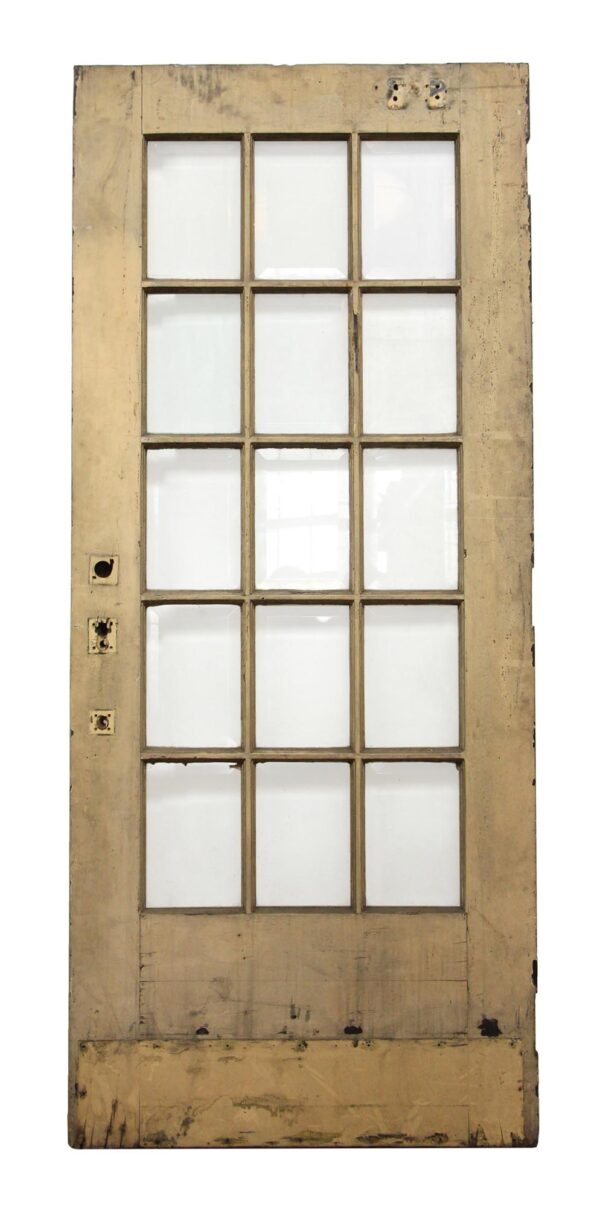 Tan French door with 15 glass panes and worn wood frame, shown front on.