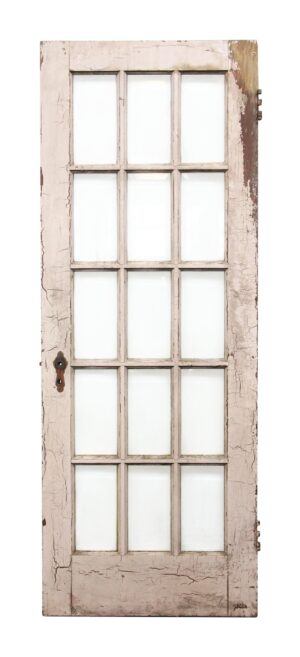 Antique French door with 15 beveled glass panes and a pink painted frame, shown with worn hardware on one edge.
