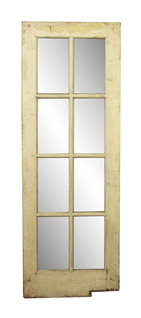 Antique wooden French door with eight glass panes and a weathered painted finish.
