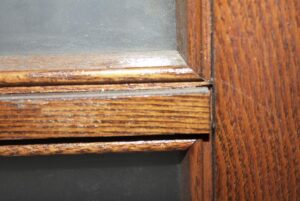 Close-up of a stained oak French door corner with trim and the edge of a glass pane visible.