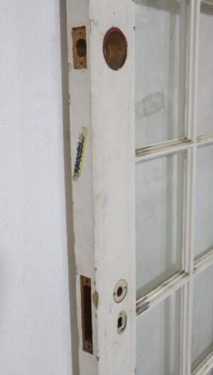 Close-up of a white wooden French door with glass panes, showing worn edge cutouts and hardware openings.