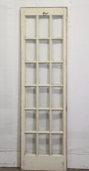 Vintage white wood French passage door with 18 glass panes and worn paint.