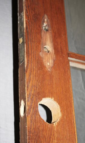 Close-up of an antique 15-lite oak French door showing the latch edge and a missing glass pane opening.