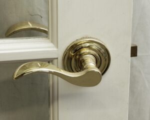 Close-up of a white wood French door showing a brass lever handle and part of a glass panel.