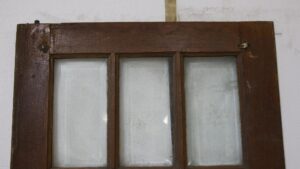 Dark wood tone French door with three vertical beveled glass lites shown in a close-up of the upper section.