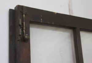 Close-up of a dark wood tone French door showing the hinge and upper frame detail.