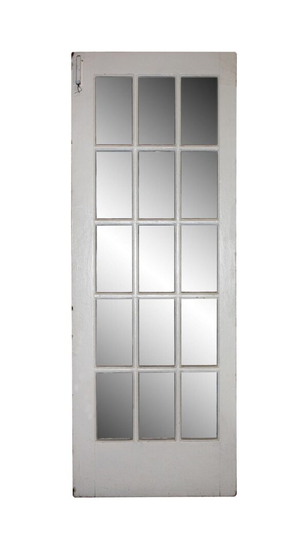 White wooden French door with 15 glass panes, shown full length, with some original hardware still attached.