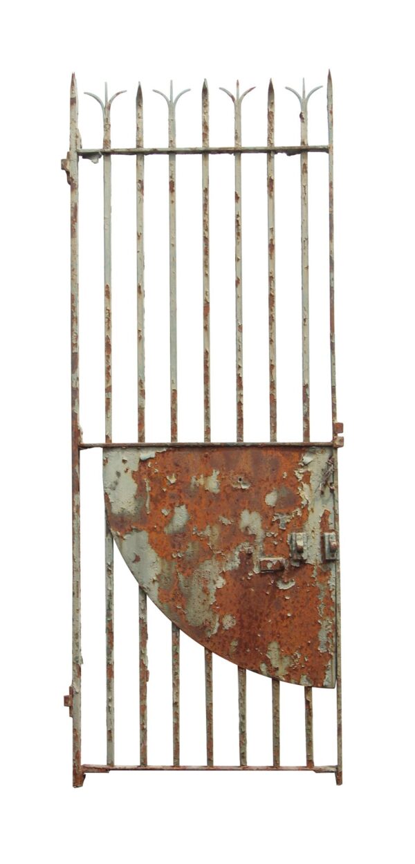 Tall wrought iron gate with split finials and a curved lower security panel, shown with distressed green paint and rust on the surface.