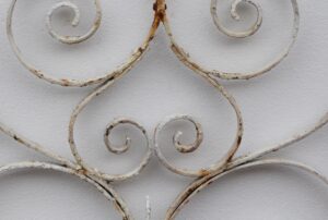 Close-up of a white wrought iron gate with curled decorative scrollwork and visible rust spots.