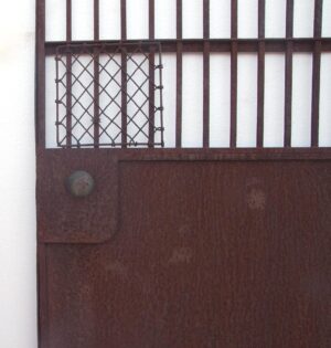 Wrought iron elevator gate with vertical bars, a lattice side section, a solid lower panel, and a round knob on the left.