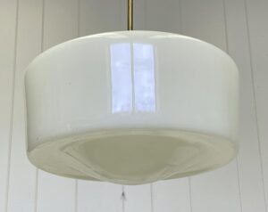 Mid-century schoolhouse pendant light with a white milk glass globe and antique brass pole fitter, shown in a close-up view of the shade and suspension rod.