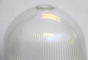 Close-up of a clear glass domed globe shade with ribbed lines and a rounded top opening.
