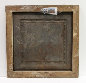 Back view of an antique tin panel painting in a worn wooden frame, with a small hanging tag taped across the top edge.