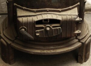 Close-up of a cast iron wood burner with a black finish, showing the front door, vent opening, and control handle.