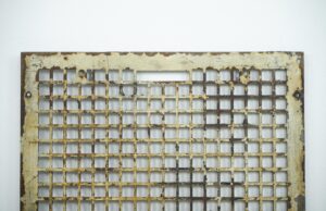Rectangular cast iron wall grate with a square grid, showing chipped white paint and surface rust, photographed from the front.