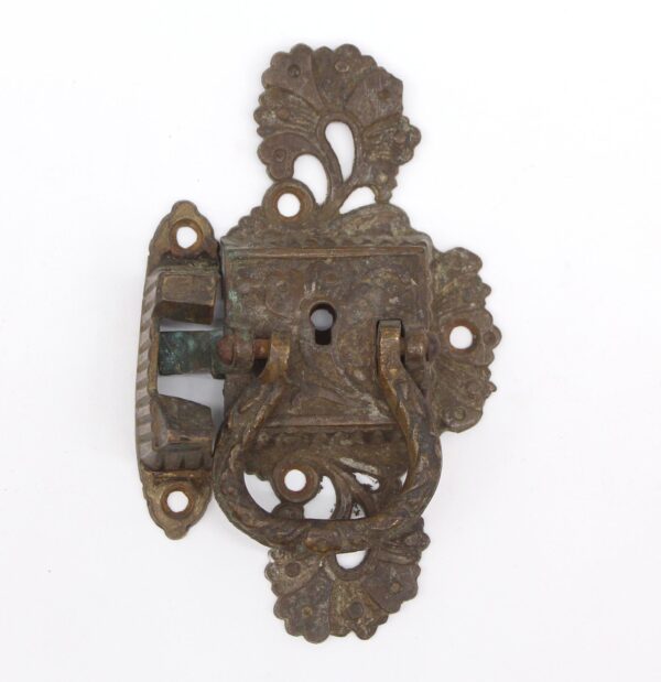 Ornate Art Nouveau bronze ice box latch with decorative cutouts and worn antique finish, shown with its mounting plate and latch mechanism.