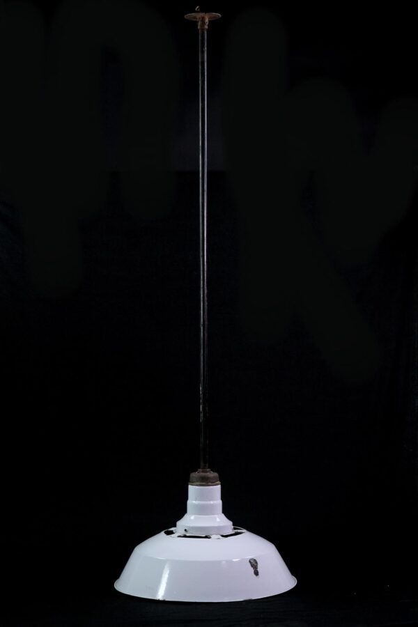 Industrial pendant light with a white enameled steel shade and a long black pole, shown against a dark background.
