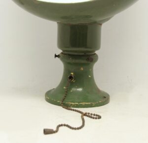 Close-up of an angled flush mount light with a green steel base and pull chain.