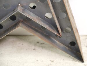 Close-up of a black metal star-shaped light frame with perforated panels and visible rust along the edges, shown without bulbs.