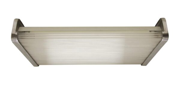 Industrial wall mount fluorescent light with a nickel Art Deco frame and clear ribbed glass lens.