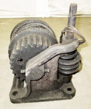 Antique industrial pulley made of cast iron with a wire rope and vertical shaft, shown in a close-up view of the mechanism.