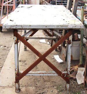 White metal industrial table with rusted cross straps and chipped paint, shown from the front.
