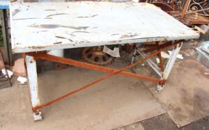 Weathered metal table with a white top, rusty cross straps, and chipped paint.