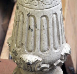 Close-up of a white cast iron staircase post with fluted detailing and chipped paint showing age.