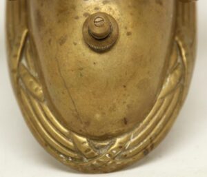 Close-up of an antique bronze Empire wall sconce showing the central socket area and part of the cast decorative frame.