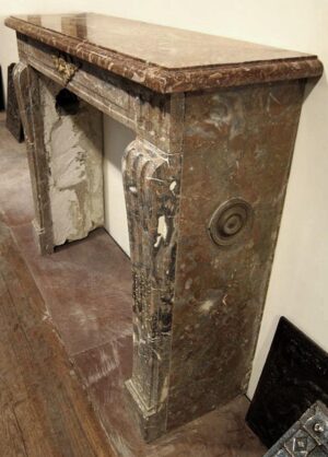 A red marble mantel with an antique bronze face, shown at an angle with the top shelf and side vent opening visible.